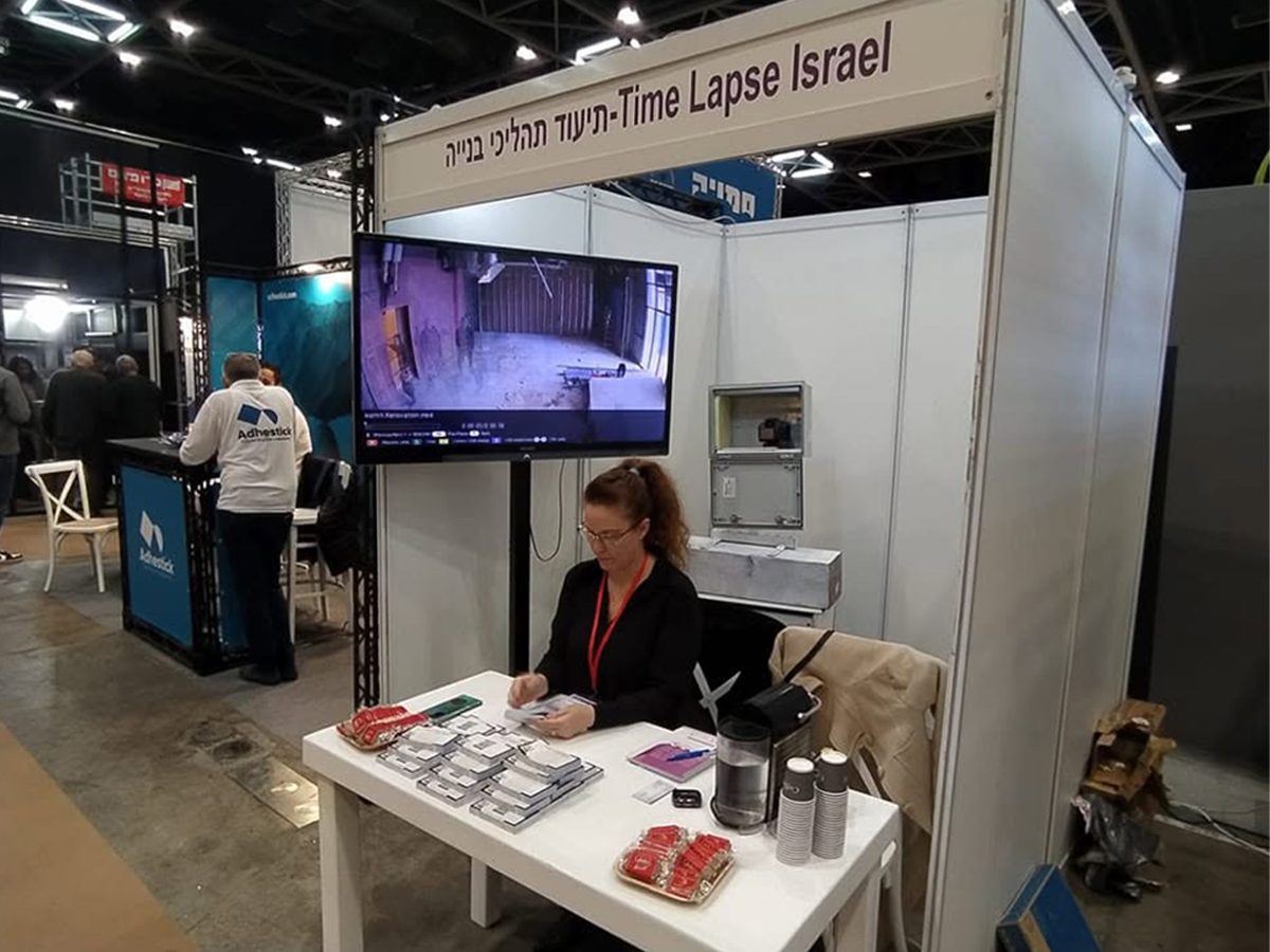 נציגת טיימלאפס ישראל בדוכן החברה בתערוכת ענף הבנייה, עם מסך המציג צילום טיימלאפס חי מאתר בנייה